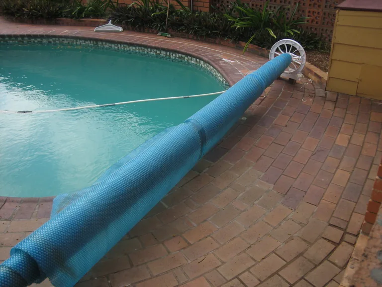 A blue bubble pool cover rolled beside a swimming pool
